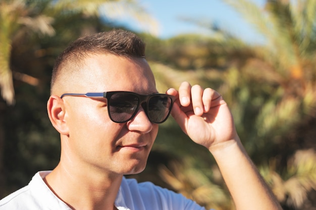 Ritratto di uomo felice bello in camicia bianca su una spiaggia di palme.