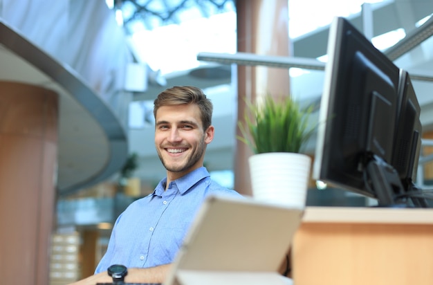 Ritratto di uomo felice seduto alla scrivania dell'ufficio, guardando la fotocamera, sorridente