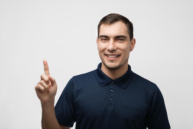 Ritratto di uomo in maglietta blu con il dito puntato su sfondo bianco per mockup pubblicitario