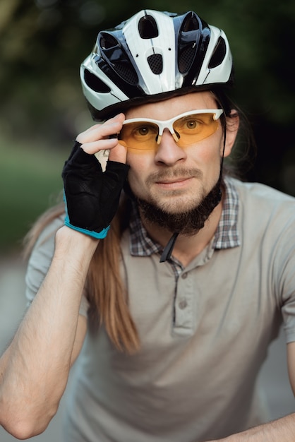 Ritratto di uomo in occhiali da sole gialli e casco in piedi con la bicicletta su strada e guardando in avanti