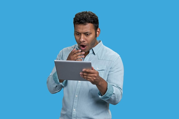 Ritratto di uomo indiano scioccato guardando lo schermo del tablet pc isolato su sfondo blu
