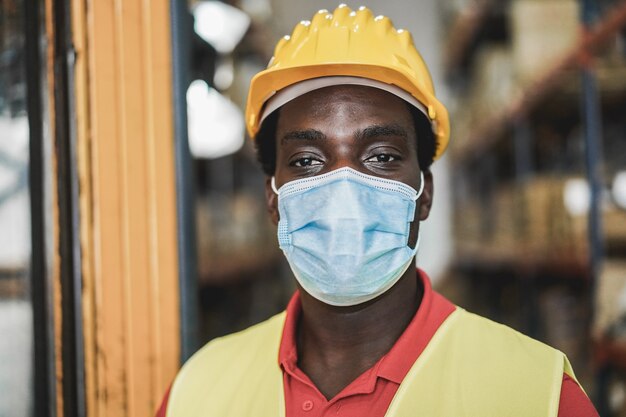 Ritratto di uomo lavoratore africano all'interno del magazzino mentre indossa la maschera protettiva - Focus sugli occhi dell'uomo