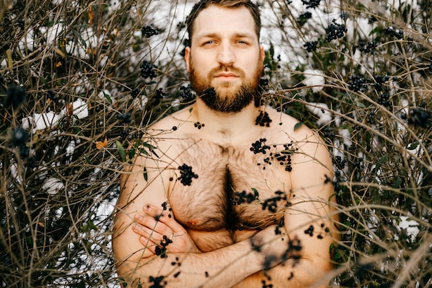 Ritratto di uomo nudo brutale allo zenzero con la barba in posa tra i cespugli