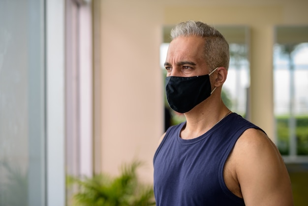 Ritratto di uomo persiano maturo con maschera per la protezione dall'epidemia di virus corona distanza sociale in palestra