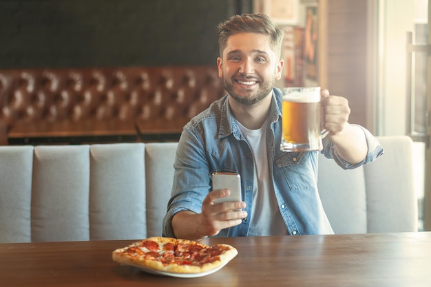 Ritratto di uomo sorridente con in mano un bicchiere di birra nella caffetteria e guardando la telecamera