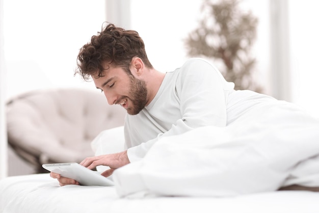 Ritratto di uomo sorridente sdraiato sul letto e con tavoletta digitale in camera da letto