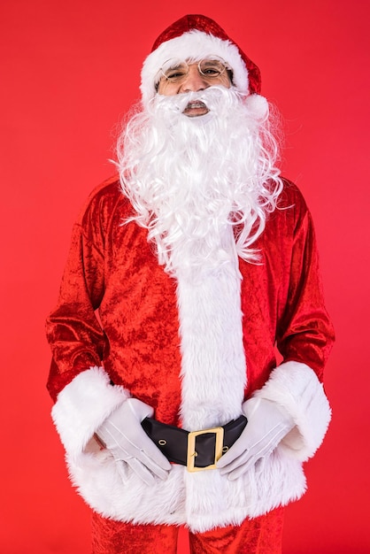 Ritratto di uomo vestito da Babbo Natale in posa per la macchina fotografica su sfondo rosso Festa di Natale regali consumismo e concetto di felicità