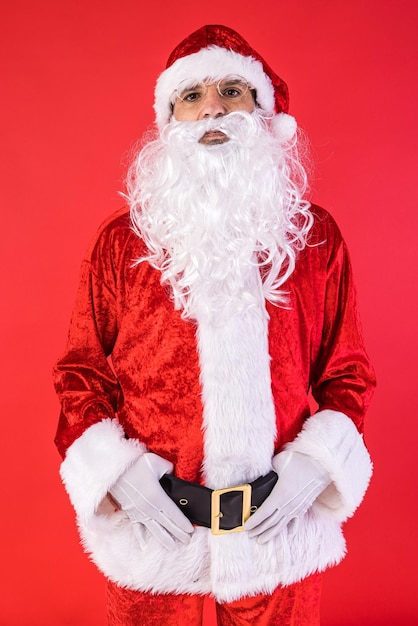 Ritratto di uomo vestito da Babbo Natale in posa per la macchina fotografica su sfondo rosso Festa di Natale regali consumismo e concetto di felicità