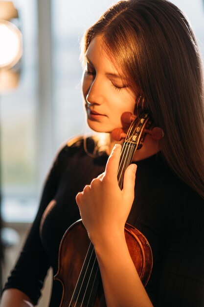 Ritratto di violinista femminile Ispirazione musicale Tranquillità mente Godersi il silenzio Elegante donna sorridente che tiene teneramente il violino nelle mani luci calde