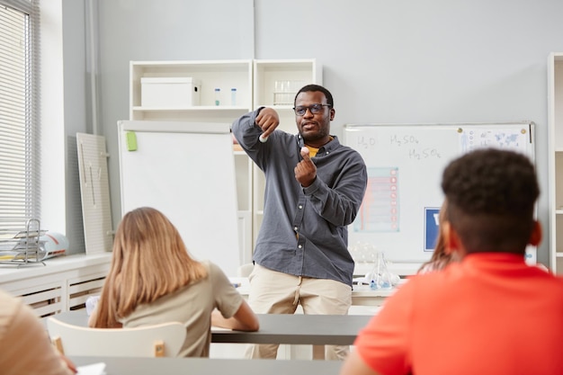 Ritratto di vista frontale dell'insegnante afroamericano che spiega la meccanica delle molecole a un gruppo di bambini in classe di chimica