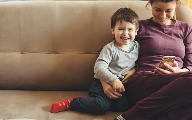 Ritratto di vista frontale di una madre caucasica e figlio seduti sul divano e utilizzando un cellulare mentre sorridono