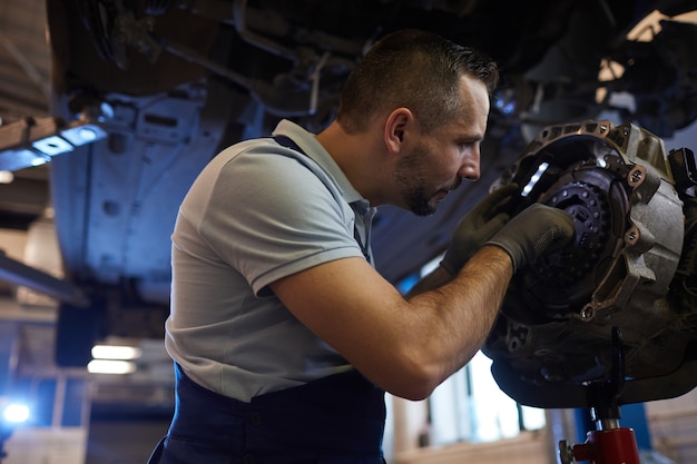 Ritratto di vista laterale del meccanico di automobile muscolare riparazione del cambio in officina automatica, copia dello spazio