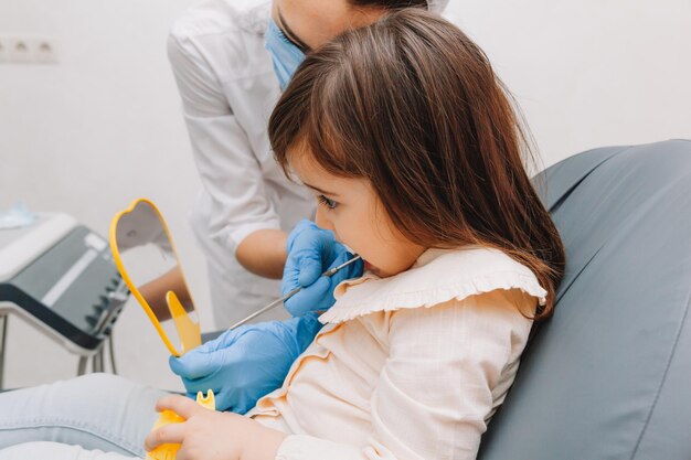 Ritratto di vista laterale della bambina che esamina specchio in odontoiatria pediatrica dopo chirurgia dentale.