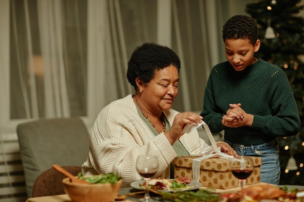 Ritratto di vista laterale della nonna afroamericana felice che apre il presente mentre si gode il natale con...