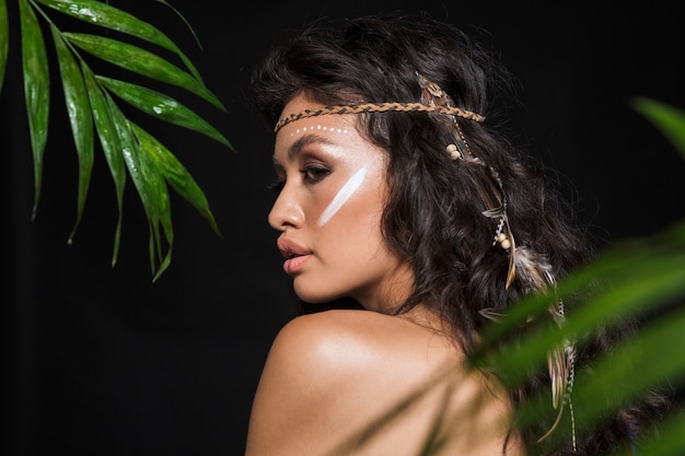 Ritratto di vista laterale di bellezza di una giovane donna bruna sensuale attraente che indossa accessori tribali in posa con foglie tropicali isolate