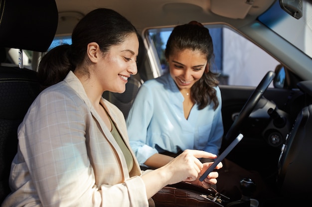 Ritratto di vista laterale di due giovani donne mediorientali che utilizzano smartphone e sorridono mentre erano seduti in macchina