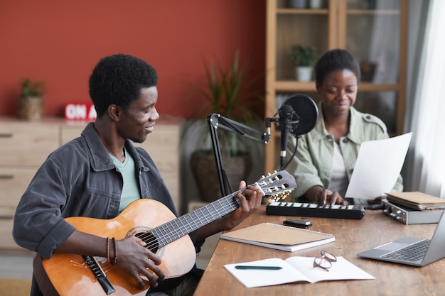 Ritratto di vista laterale di giovane uomo afro-americano a suonare la chitarra acustica durante la composizione di musica in studio di registrazione domestica, copia dello spazio