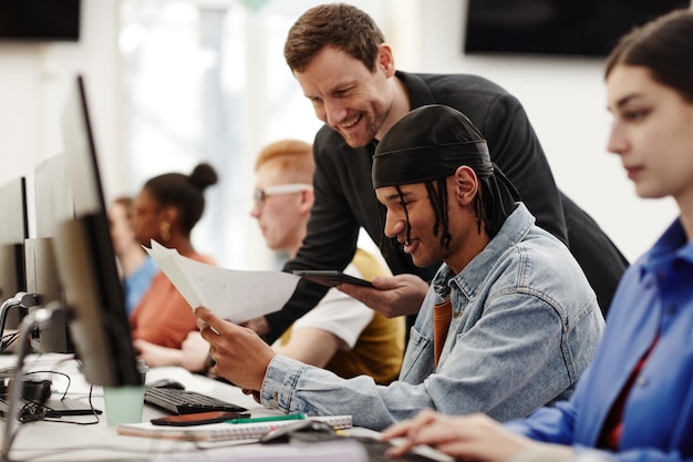 Ritratto di vista laterale di un insegnante maschio che aiuta uno studente afroamericano a utilizzare il computer in classe universitaria