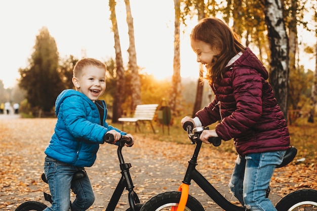 Ritratto di vista laterale di un simpatico fratello e sorella seduti faccia a faccia con le loro biciclette ridendo all'aperto nel parco.