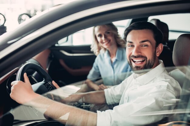 Ritratto di vista laterale di una coppia sorridente seduta in un'auto nuova e guardando la telecamera