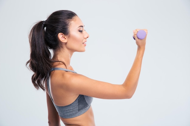 Ritratto di vista laterale di una donna felice di forma fisica che risolve con i dumbbells isolati su una parete bianca