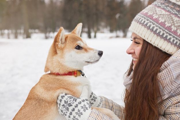 Ritratto di vista laterale di una giovane donna sorridente che tiene in mano un cane carino mentre si gode una passeggiata insieme all'aperto in inverno