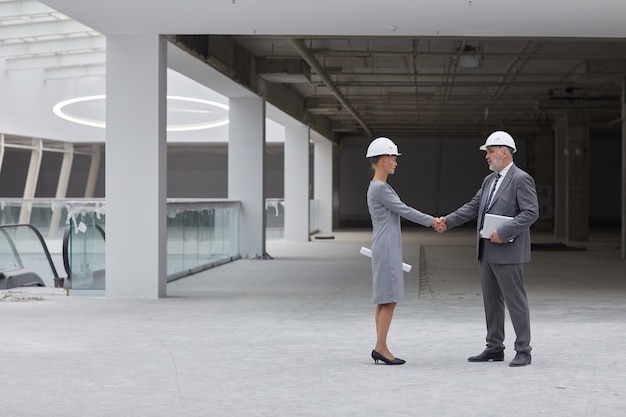 Ritratto di vista laterale integrale della donna di affari sorridente che stringe la mano con il partner dopo l'affare di investimento al cantiere,