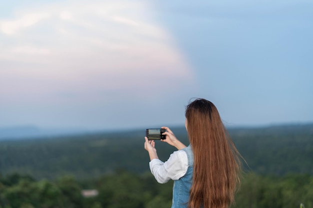 Ritratto di vista posteriore di una donna che scatta foto di un paesaggio con uno smartphone