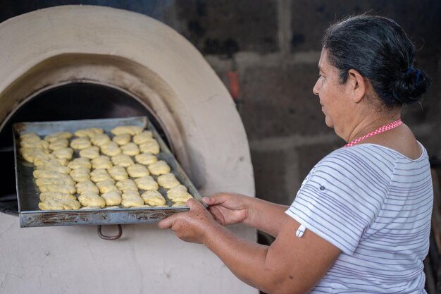 Ritratto di vista posteriore di una donna latina invecchiata che prepara pasticcini su un forno rurale