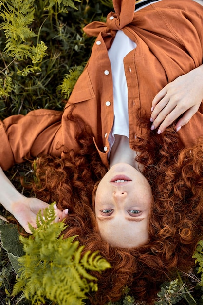 Ritratto di vista superiore della bella signora lentigginosa caucasica sdraiata sull'erba verde in estate, donna con capelli ricci rossi naturali sta cercando affascinante e sognante, godendosi il tempo nella natura. Persone, concetto di bellezza