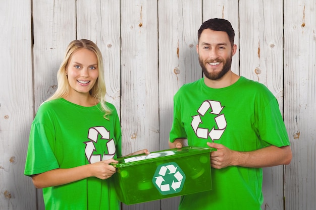 Ritratto di volontari sorridenti che trasportano il contenitore di riciclaggio su sfondo di legno