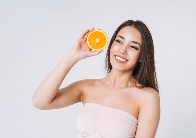 Ritratto divertente di bellezza della donna asiatica sorridente felice con capelli lunghi scuri con le arance in mani su fondo bianco isolato