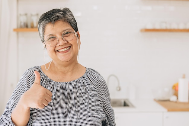 Ritratto donna asiatica matura in buona salute felice sorridente carino bella a casa cucina mano pollici in su