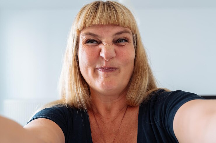 Ritratto donna di mezza età bionda che fa smorfie davanti allo specchio