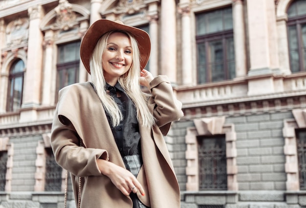 Ritratto drammatico di una donna alla moda con un cappotto e un cappello autunnali su sfondo di architettura urbana