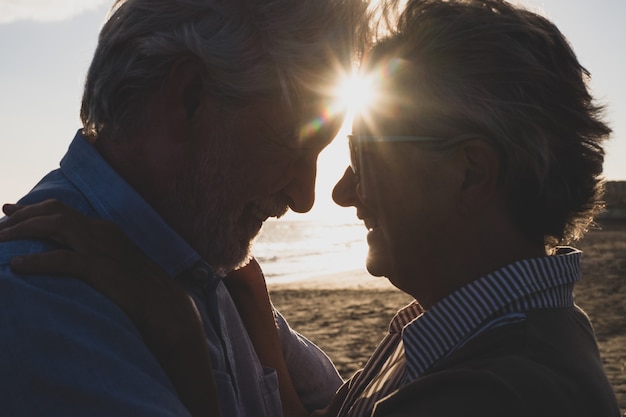 Ritratto e primo piano di due anziani innamorati felici che ballano sorridendo con il sole del tramonto tra le loro teste