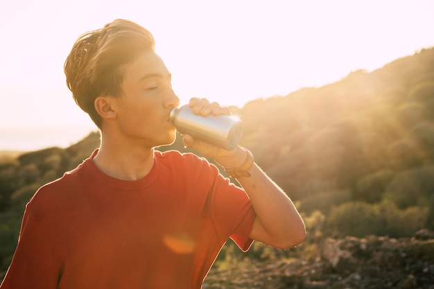 Ritratto e primo piano di un giovane o di un adolescente che beve acqua e si idrata con l'acqua la sera con il tramonto sullo sfondo