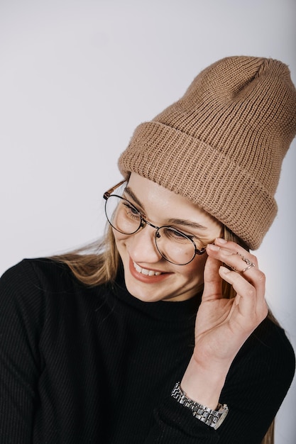 Ritratto emotivo candido inalterato di giovane donna felice con capelli lunghi biondi su fondo grigio. Colpo dello studio della ragazza alla moda casual hipster in berretto lavorato a maglia.