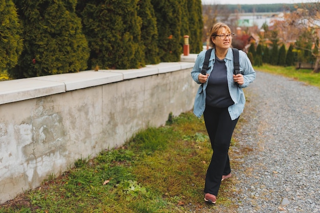 Ritratto esterno di felice pensionata europea con zaino che si gode la splendida natura mentre cammina nordico Persone anziane stile di vita attivo e concetto di salute