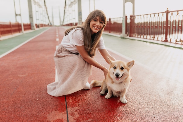 Ritratto esterno di sorridente bella signora che cammina con un cane in città alla luce del sole