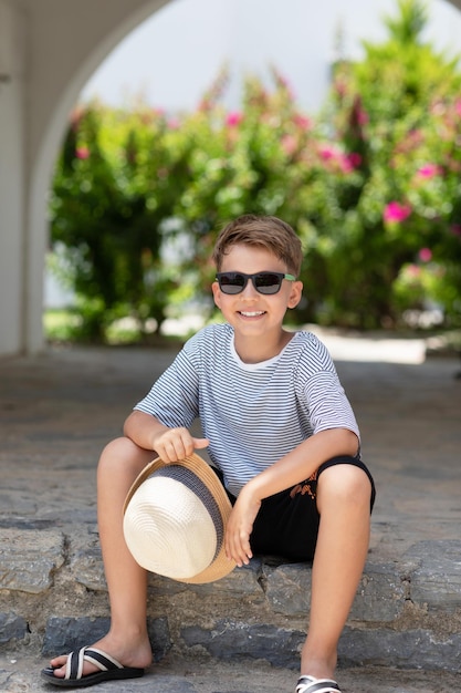 Ritratto esterno verticale di un bel ragazzo estivo in una giornata di sole Scolaro sorridente felice in maglietta a righe e occhiali da sole in posa guardando alla fotocamera