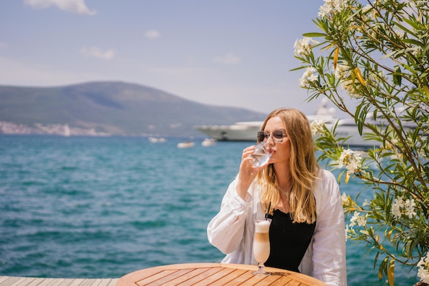 Ritratto estivo mediterraneo di vacanza di donna elegante in posa allo yacht club Montenegro che beve caffè e si rilassa