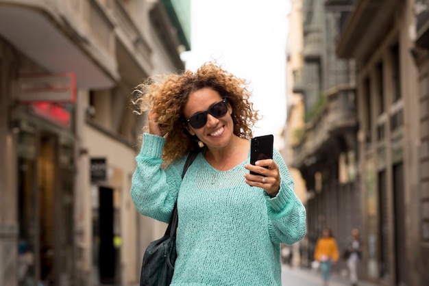 Ritratto f allegra adulta bella donna fare telefonata con la moderna tecnologia cellulare camminando per la strada nel concetto di città di attività per il tempo libero luogo urbano all'aperto e gente alla moda sorridente