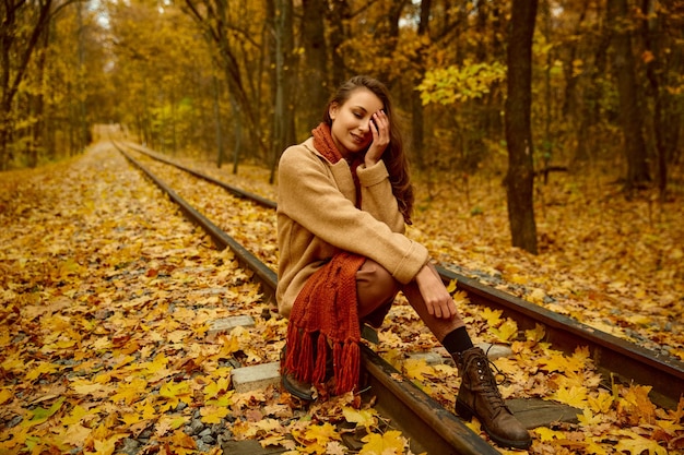 Ritratto femminile autunnale. Donna premurosa pensierosa che si siede sulla testa della holding del binario ferroviario