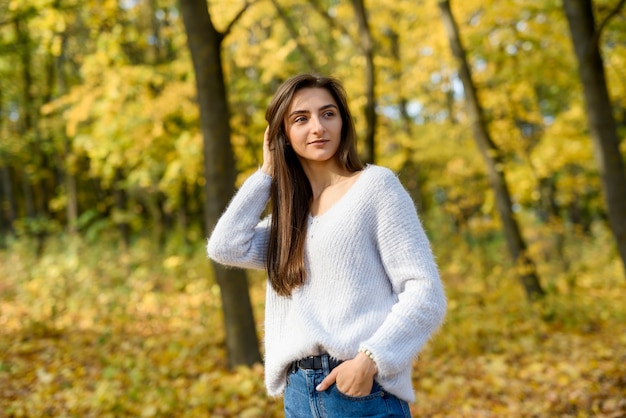 Ritratto femminile. Giovane donna in abbigliamento casual in posa nella foresta autunnale con foglie gialle