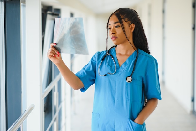 Ritratto fiducioso afroamericano medico femminile medico professionista scrittura note paziente isolate su priorità bassa di finestre corridoio clinica ospedale. Espressione positiva del viso