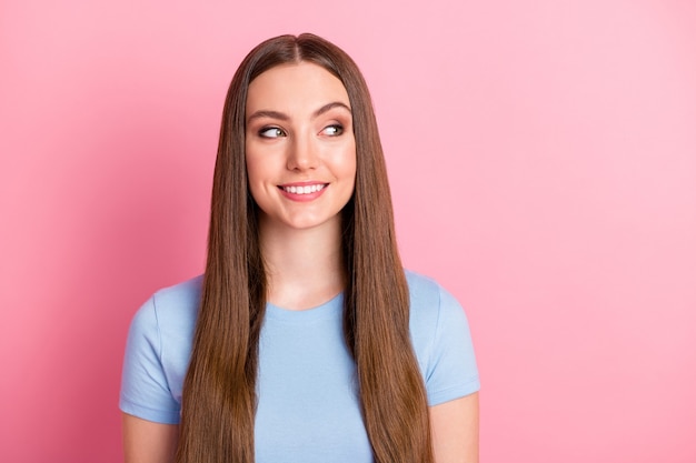 Ritratto fotografico di una ragazza curiosa con lunghi capelli castani che sorride guardando uno spazio vuoto isolato su uno sfondo di colore rosa pastello