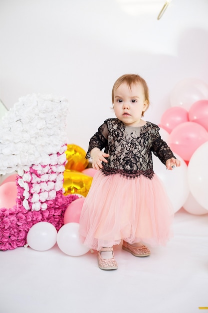 Ritratto fotografico di una ragazza di compleanno di 1 anno in un abito rosa con palloncini rosa. Il bambino in vacanza sorride, le emozioni dei bambini. Festa di compleanno