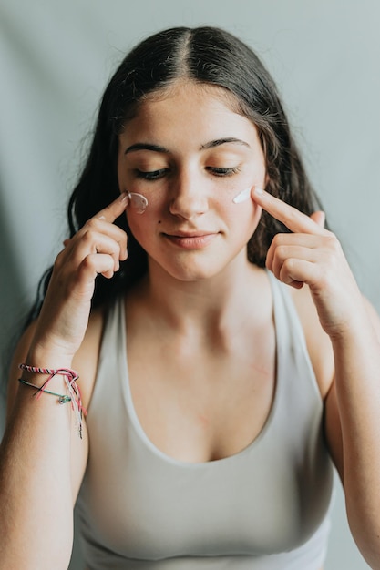 Ritratto gioioso e divertente di una giovane donna adulta con crema lozione sulle guance Cura della pelle bellezza viso e donna con crema per dermatologia acne e bagliore su sfondo studio