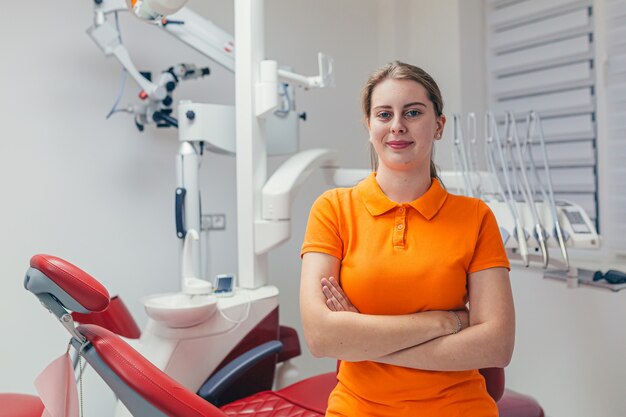 ritratto giovane amichevole femmina dentista sorridente e guardando davanti in un moderno studio dentistico